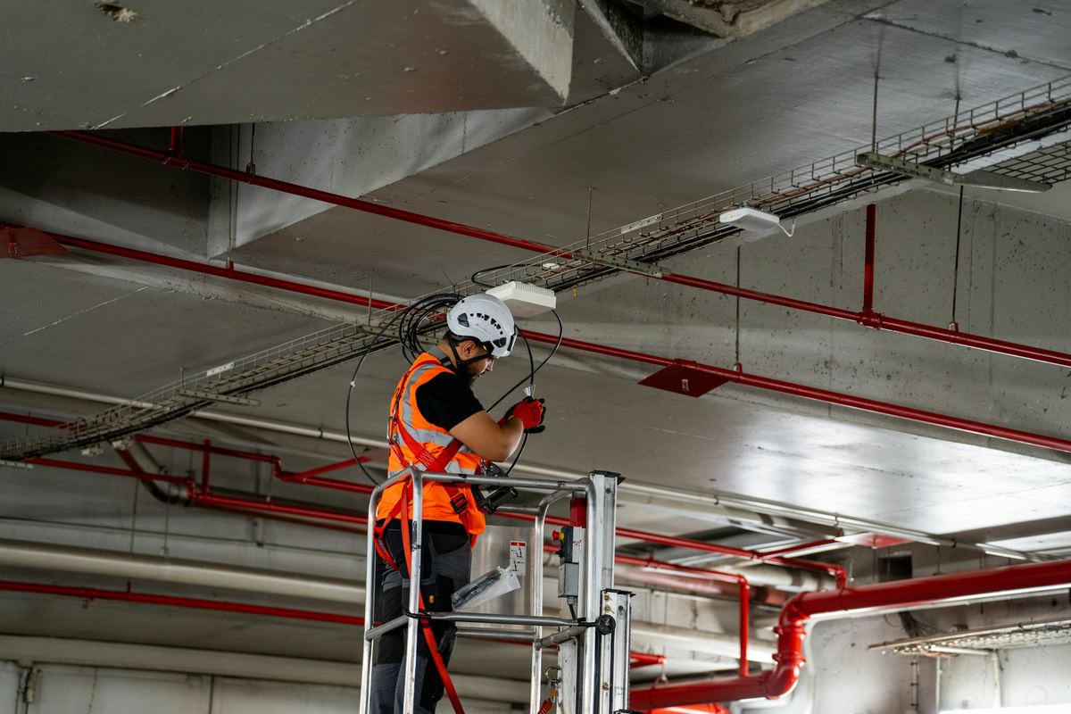 Een technicus op een hoogwerker maakt een kabel klaar onder een kabelgoot